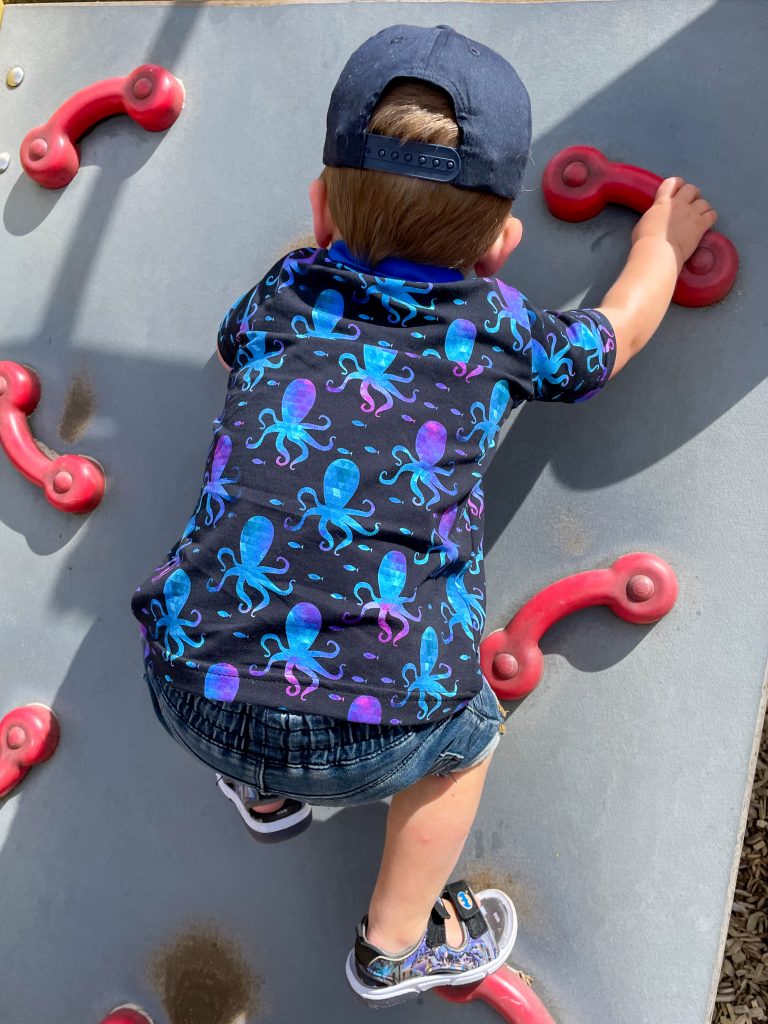 little boy in dark blue polo shirt with octopus print climbing wall