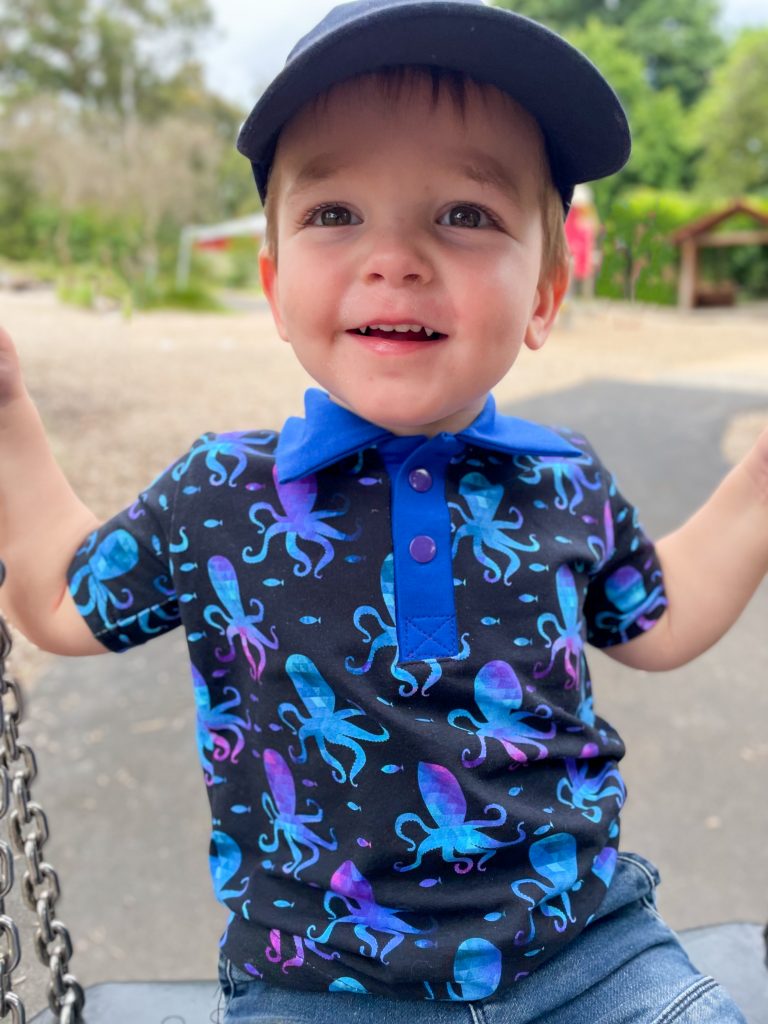 little boy in dark blue polo shirt with octopus print smiling on a swing