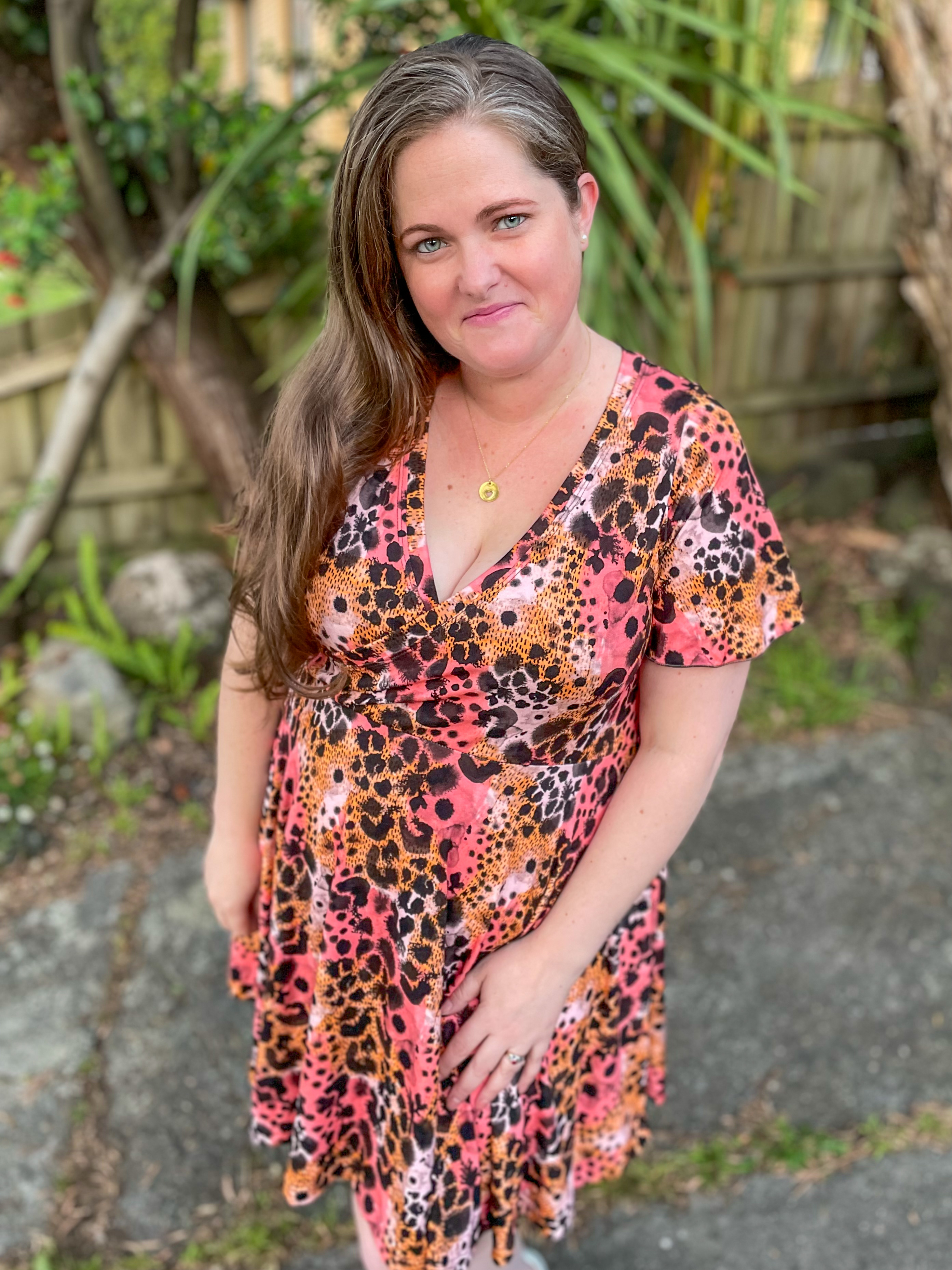 A woman in a leopard print dress smirks for a photo while standing outdoors